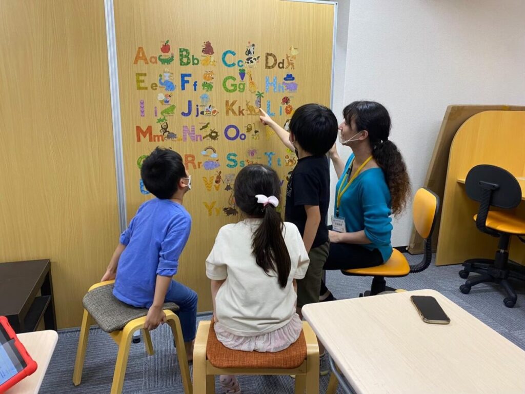 アクティビティで子どもたちが講師とアルファベット表を見ながら学ぶ様子